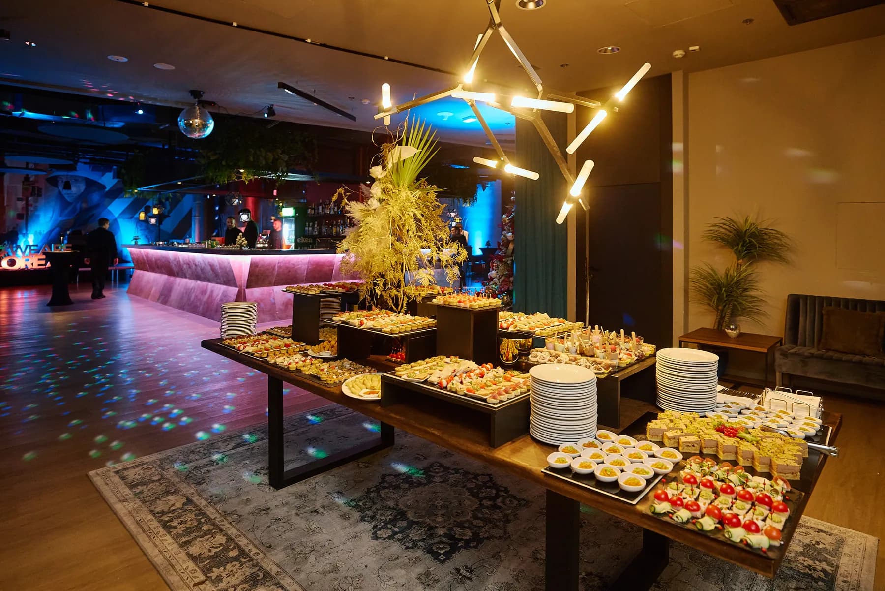 WESPA event space in Zagreb set up for a company event: a long catering table with canapés under a modern chandelier, a lit pink bar and a dance floor with disco lights